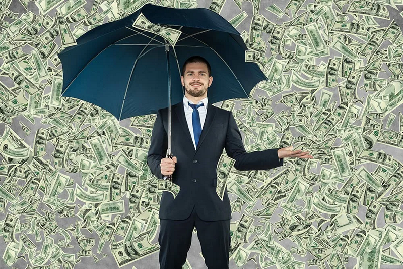 A man in a suit stands under an umbrella surrounded by falling dollar bills.