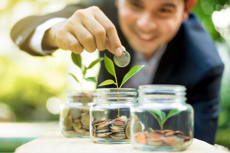 A person adding a coin to a jar with a growing plant, symbolizing financial growth and investment.